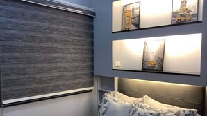 A bedroom with a bed, a window with blinds, and three framed pictures on the wall.