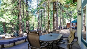 Een terras buiten met een ronde tafel en stoelen, omringd door hoge bomen.