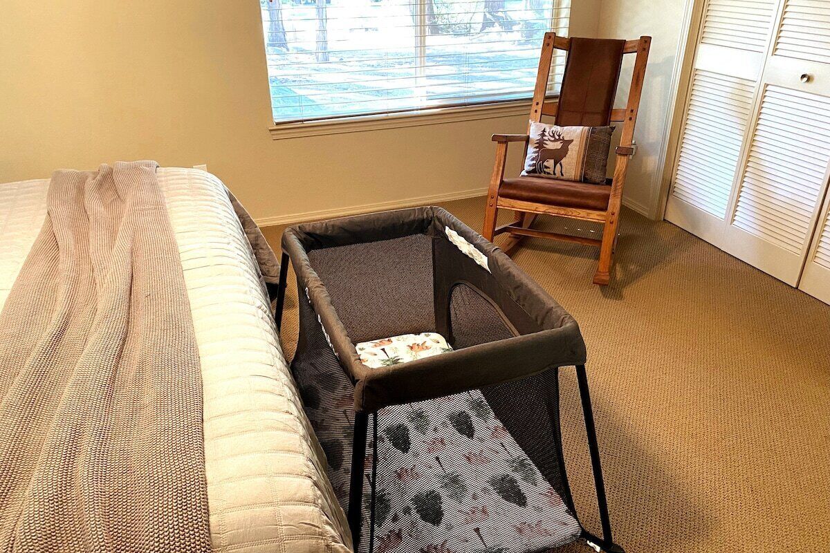 A bedroom with a bed, a small chair with a cushion, and a window with blinds.