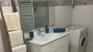 Un bany amb un lavabo blanc, un mirall, una màquina de rentar i una catifa blava.