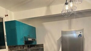 Eine Küche mit türkisfarbenen Schränken, einem Edelstahl-Kühlschrank, einem Gasherd und einer Pendelleuchte.