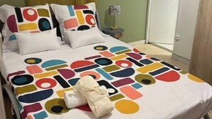 Ein Bett mit einer farbenfrohen Bettdecke mit geometrischem Muster, einem weißen Kissen und einem gefalteten weißen Handtuch.