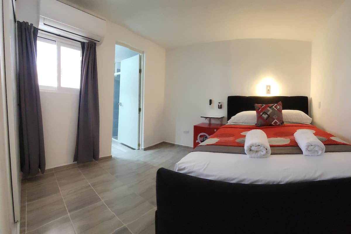 Habitación de hotel con cama, mesita de noche, lámpara y ventana con cortinas.