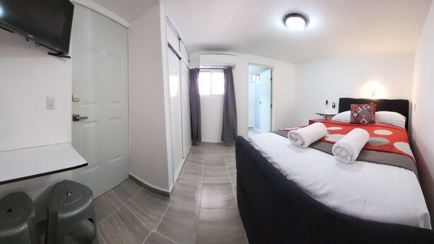 Quarto de hotel com cama, televisão, escrivaninha e banheiro.