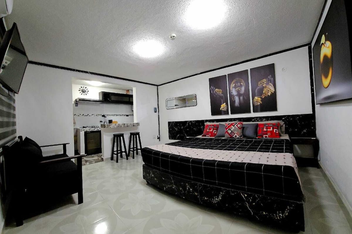 Una habitación compacta con una cama, un pequeño espacio kitchenette y un televisor montado en la pared.
