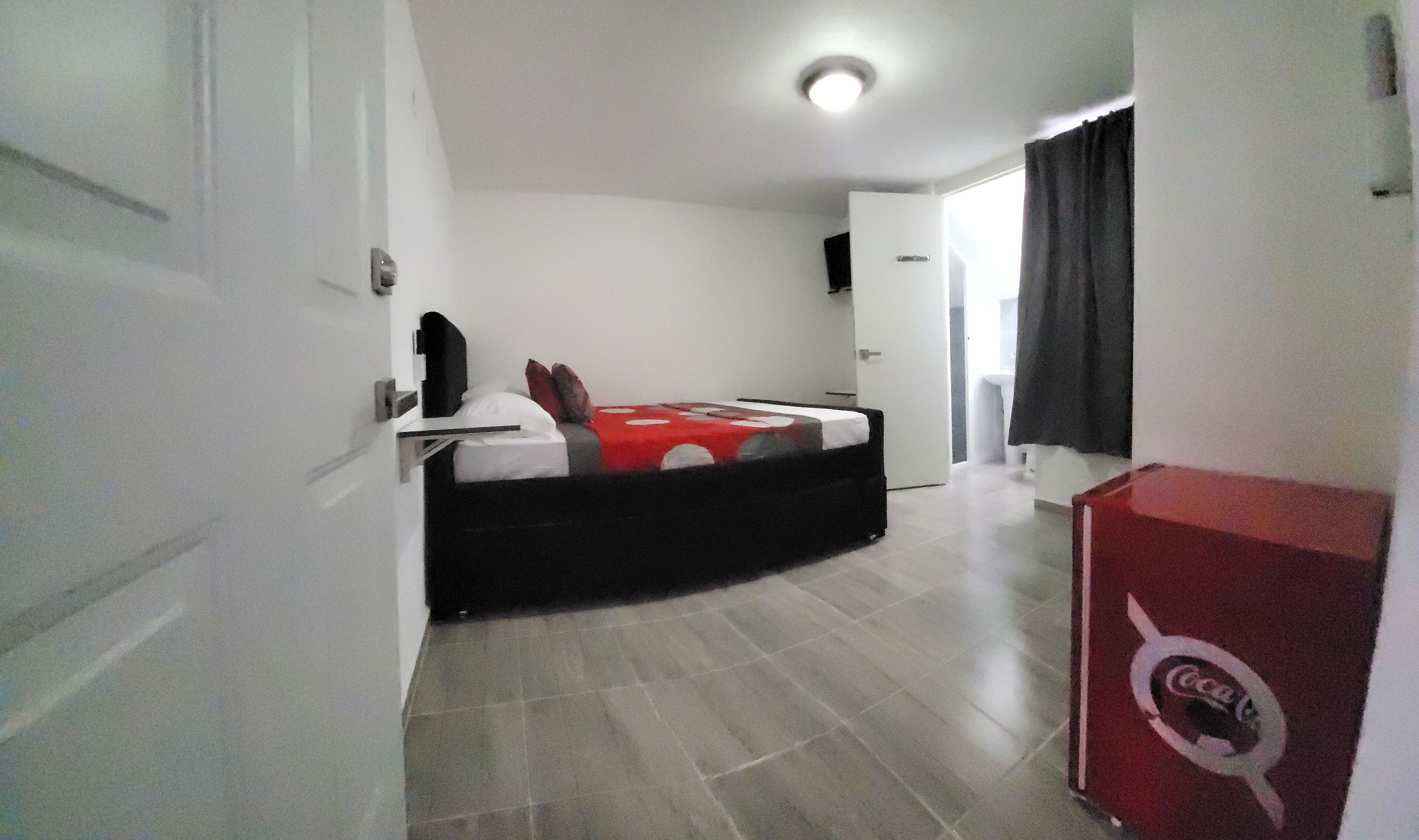 Une chambre avec un lit, une armoire, une porte et un réfrigérateur rouge de la marque Coca-Cola.