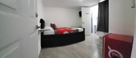 Une chambre avec un lit, une armoire, une porte et un réfrigérateur rouge de la marque Coca-Cola.