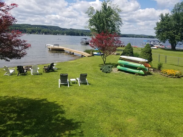 Un patio junto al lago con sillas de jardín, un muelle y kayaks.