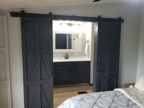Un dormitorio con cama, un espejo grande, un lavamanos y puertas de madera oscura.