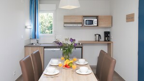 A modern kitchen with a microwave, coffee maker, and a dining area with a table set for two, including plates, cups, and a fruit bowl.