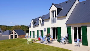 A row of white buildings with green shutters, a grassy lawn, and outdoor seating.