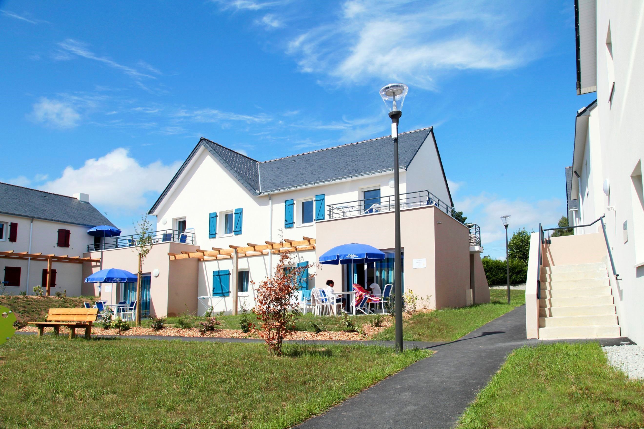 A modern building with a covered outdoor seating area, a pathway, and a staircase leading to an upper level.