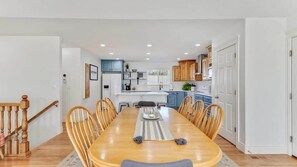 A dining area with a wooden table, chairs, and a kitchen in the background. - The Gathering Place for Paws, Friends, and Family (Orem)