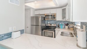 A modern kitchen with white cabinets, stainless steel appliances, a toaster, and a tiled backsplash. - Seaglass Shores, Steps to the Beach (Cape Canaveral)