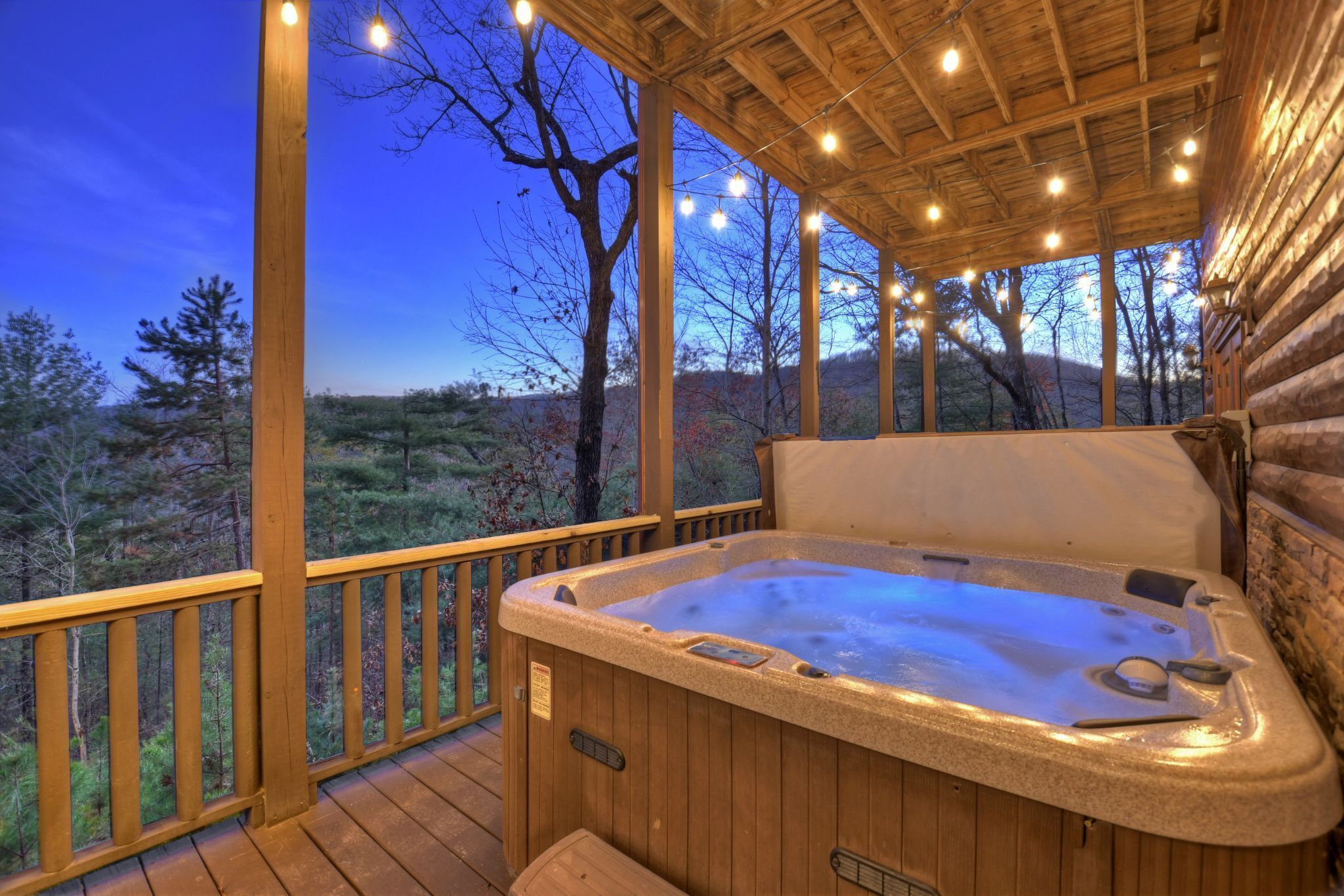 A wooden deck with a hot tub, wooden railings, and a view of the surrounding forest.