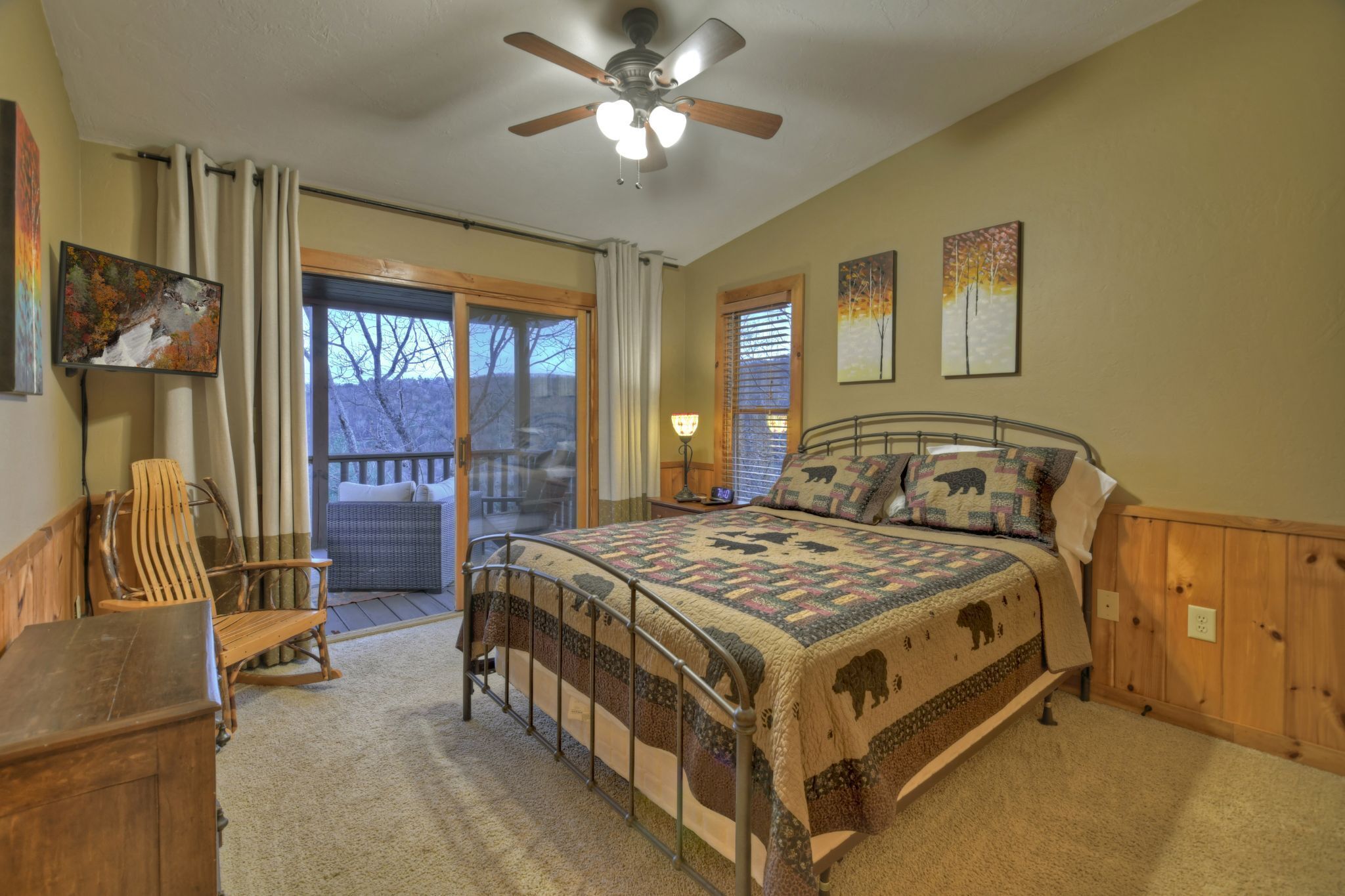 A bedroom with a bed, a chair, a desk, a ceiling fan, and a view of the outdoors.