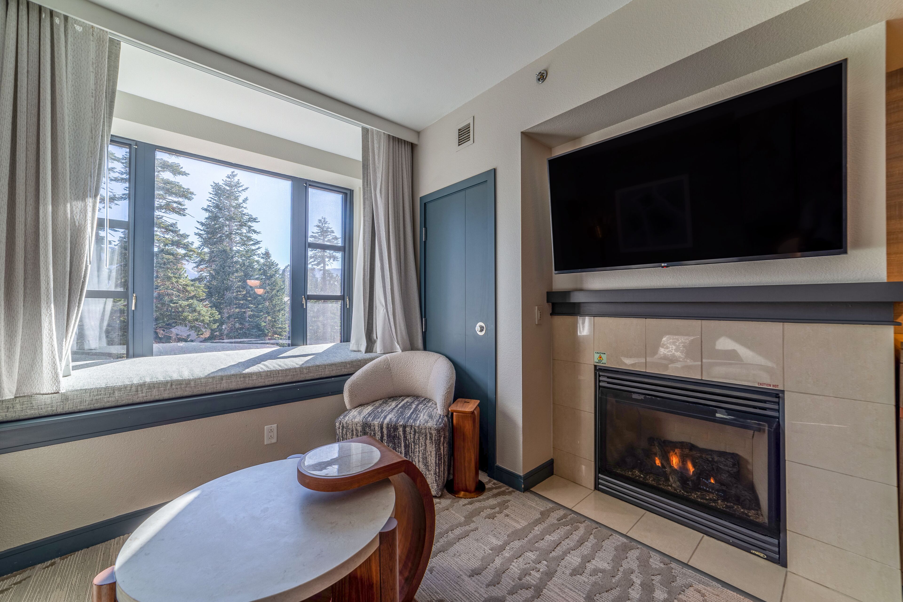 A cozy living room with a fireplace, a television mounted above it, a comfortable chair, and a dining table.