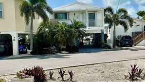 A two-story residential building with a covered front porch, palm trees, and a driveway.