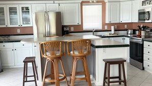 A modern kitchen with white cabinets, a central island with stools, a ceiling fan, and a microwave.