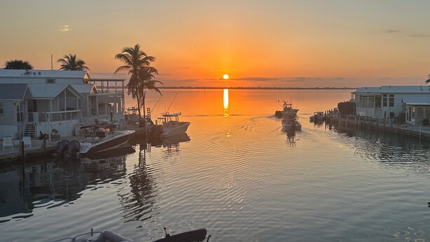 A marina with boats docked, a sunset, and buildings with balconies.