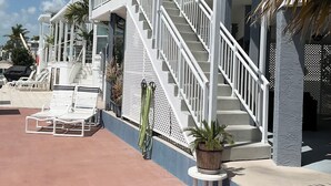 A beachfront property with a covered patio, white railings, and a staircase leading to an upper level.
