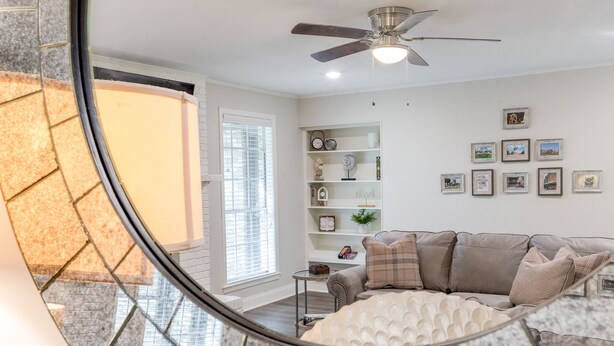 Un salon moderne avec un ventilateur de plafond, un canapé, une table basse et une bibliothèque.