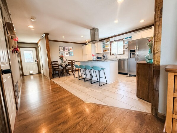 A modern kitchen with wooden flooring, a central island with bar stools, and a stainless steel refrigerator.
