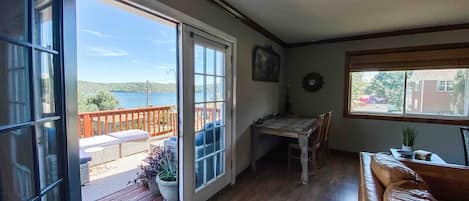 A room with a wooden floor, a brown leather sofa, a dining table with chairs, and a view of a lake through a sliding glass door.