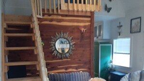 A loft-style room with a wooden staircase, a patterned sofa, and a decorative mirror on the wall.