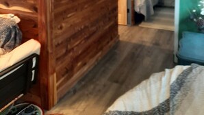 A room with wooden paneling, a bed with a patterned blanket, and a small table with a decorative item.