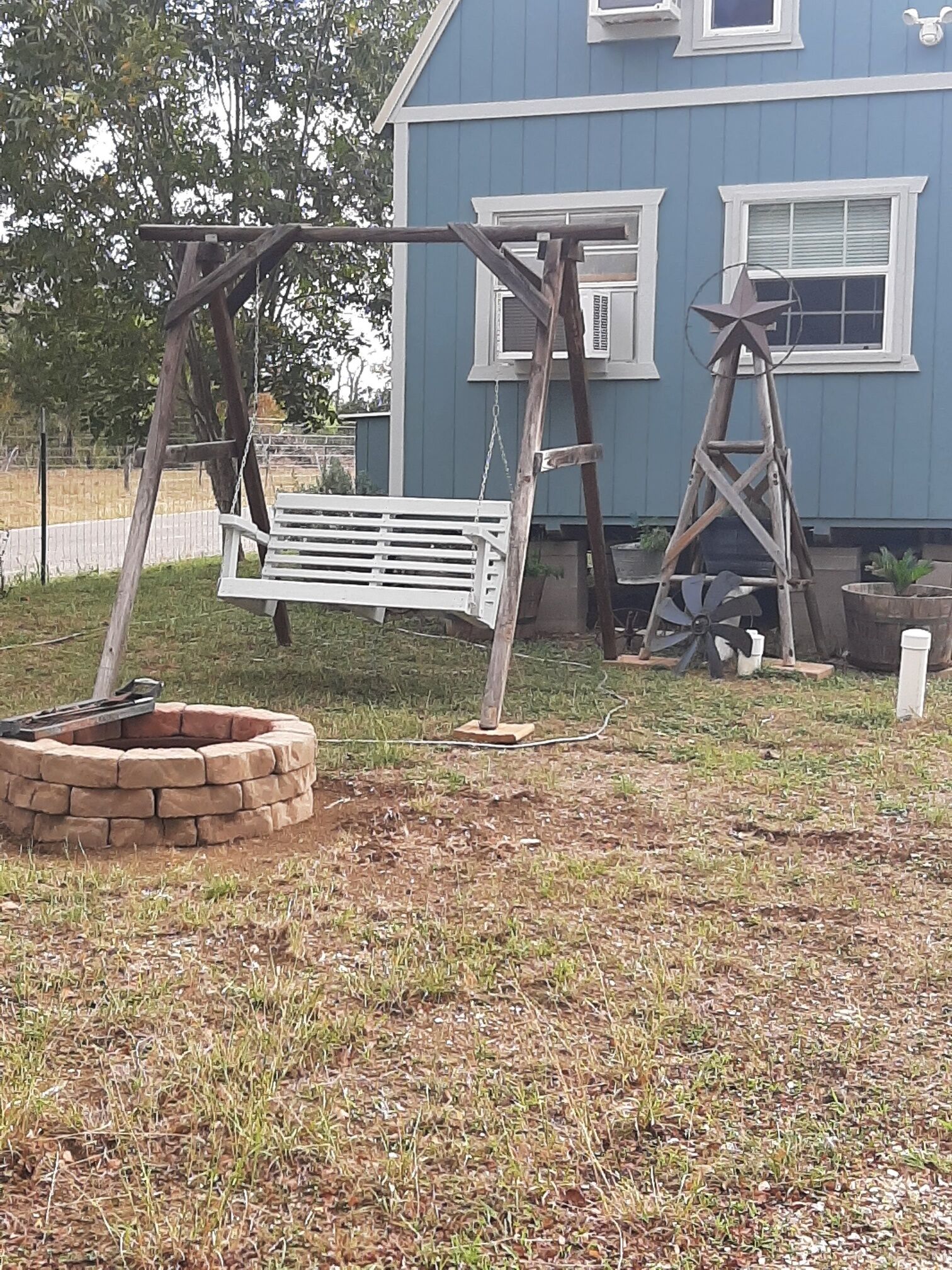 A backyard with a swing set, a fire pit, and a ladder.