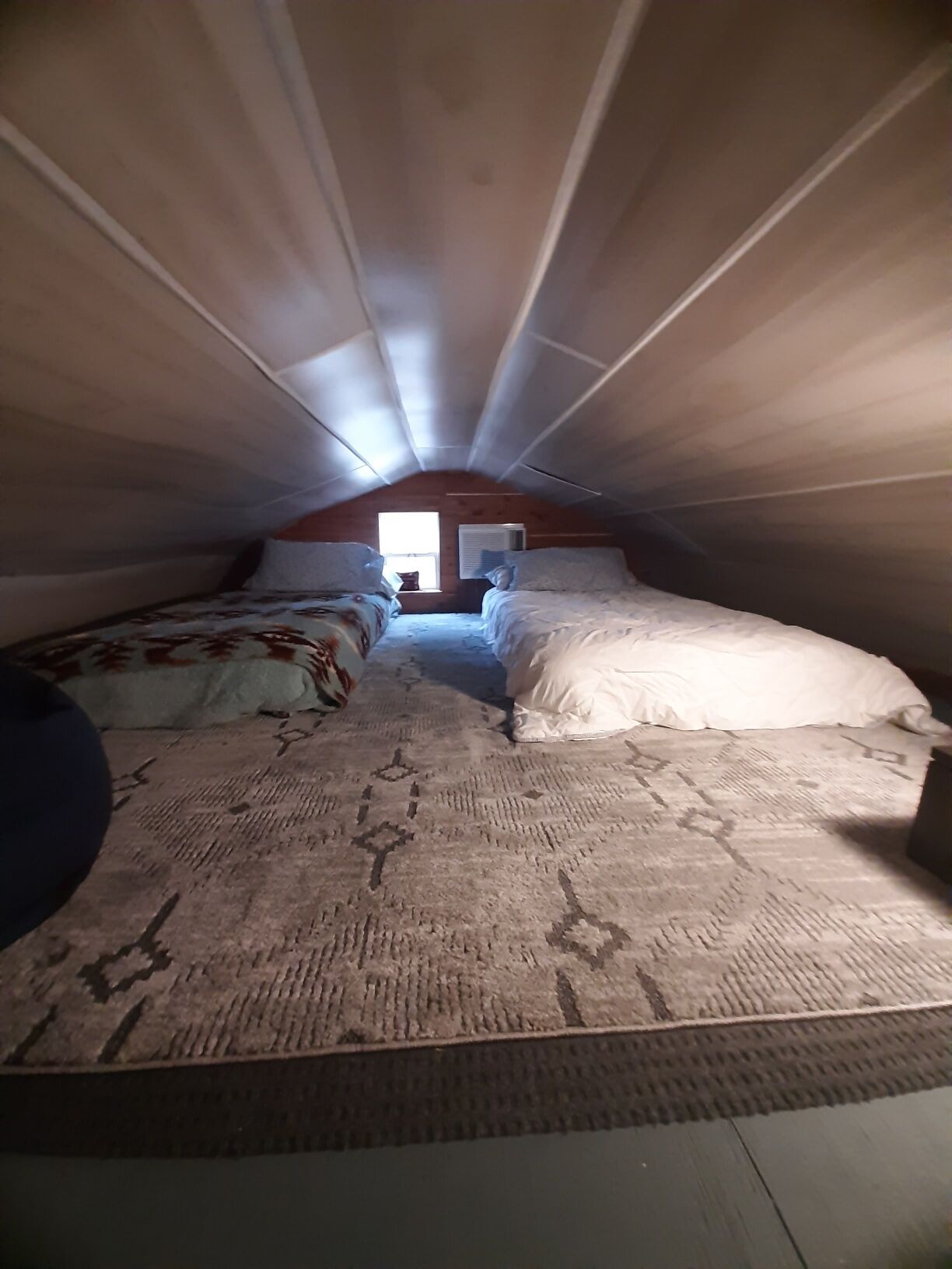 A small attic bedroom with two beds, a window, and an air conditioning unit.