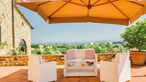 Un espace extérieur aménagé avec des sièges, un bâtiment en pierre, un grand parasol et une vue sur la campagne.