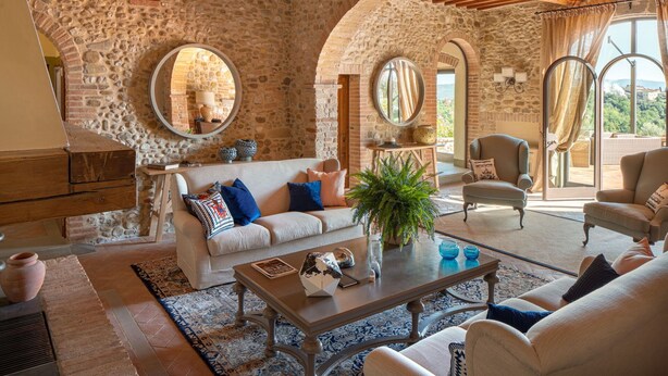 Un salon spacieux aux murs en pierre, avec un canapé blanc, une table basse et une vue sur l’extérieur.