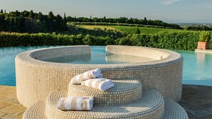 Un jacuzzi circulaire, dont l’extérieur est recouvert de carreaux, est entouré d’une piscine. Des serviettes sont disposées sur les marches menant au jacuzzi.