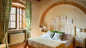 Une chambre à coucher comprenant un lit, deux tables de chevet, une chaise, un radiateur et une fenêtre avec des rideaux.