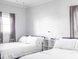 Ein Hotelzimmer mit zwei Betten, einem Nachttisch mit Lampe und einem Fenster mit Vorhängen.