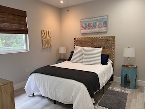 Een slaapkamer met een bed, twee nachtkastjes, een raam met een zonwering, een wanddecoratie en een schilderij.
