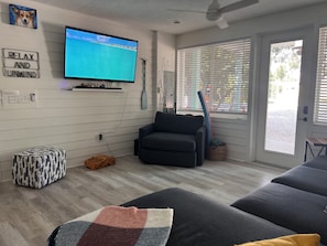 Een moderne woonkamer met een flatscreen televisie, een comfortabele bank, een gestreept voetenbankje en een ontspannen sfeer.