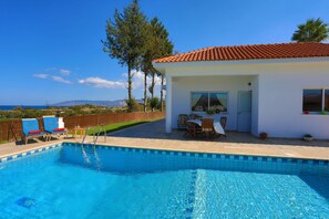 Une piscine avec des chaises longues, une terrasse avec une table et des chaises, et une vue sur la mer.