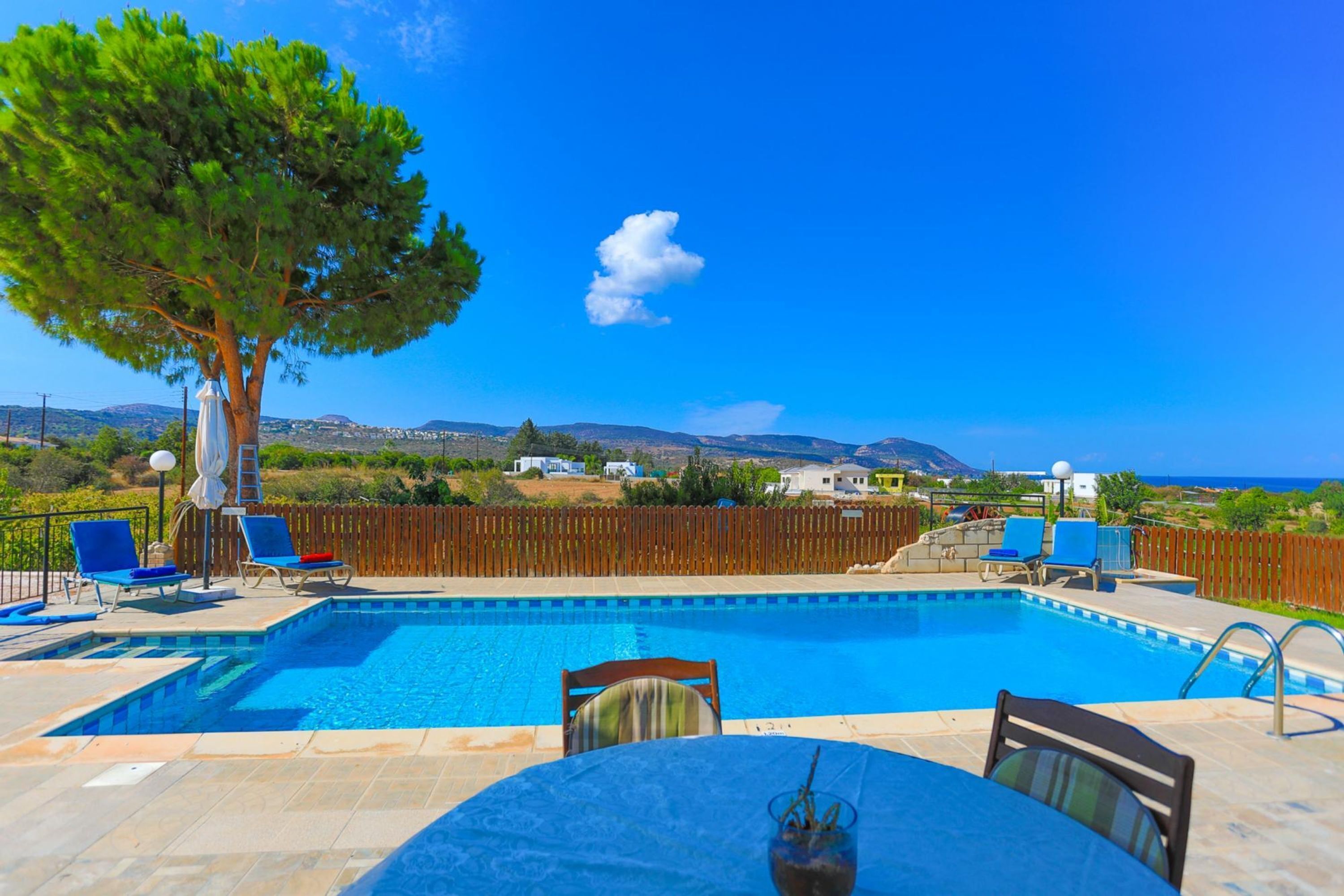 A swimming pool with a view of the sea, surrounded by lounge chairs and a table.