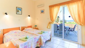 A room with two beds, a table with chairs, and a view of the outdoors through a sliding glass door. - The Vines in Latchi With 3 Bedrooms and 3 Bathrooms (Neo Chorio)