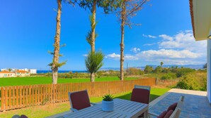 A patio with a table and chairs, a wooden fence, and a view of the sea and mountains. - The Vines in Latchi With 3 Bedrooms and 3 Bathrooms (Neo Chorio)