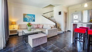 A modern living room with a sofa, coffee table, and a staircase leading to a kitchen area. - Sunny Villa Grande in Kassandra (Kassandra)