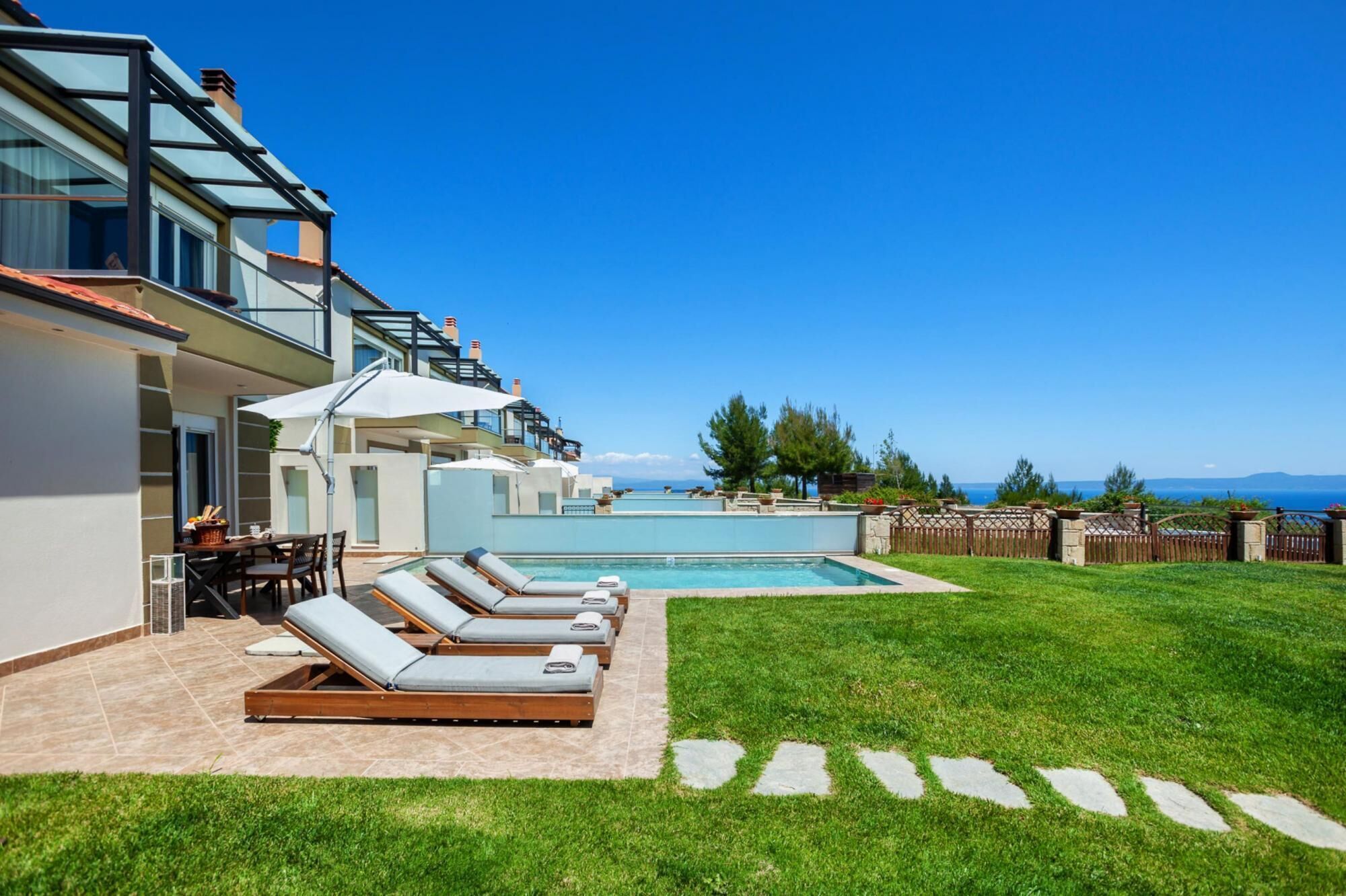 A modern pool area with lounge chairs, a clear view of the sea, and a well-maintained lawn.