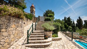 A stone staircase leading to a tower with a red dome, surrounded by greenery and a clear blue sky. - Villa Katerini in Paxi (Paxos)