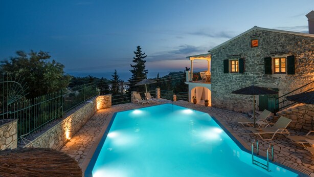A swimming pool with stone walls and a stone deck, surrounded by lounge chairs and umbrellas. - Villa Katerini in Paxi (Paxos)