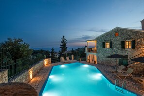 Una piscina con pareti e solarium in pietra, circondata da lettini e ombrelloni.