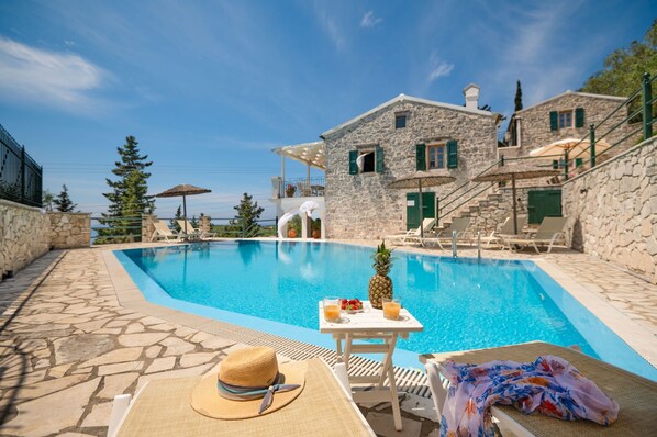 A stone building with a pool, lounge chairs, and a table with drinks and fruit.