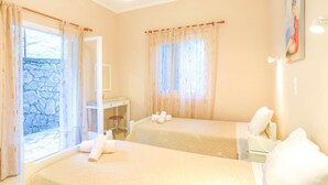 A hotel room with two beds, a desk, and a stone wall visible through the window.